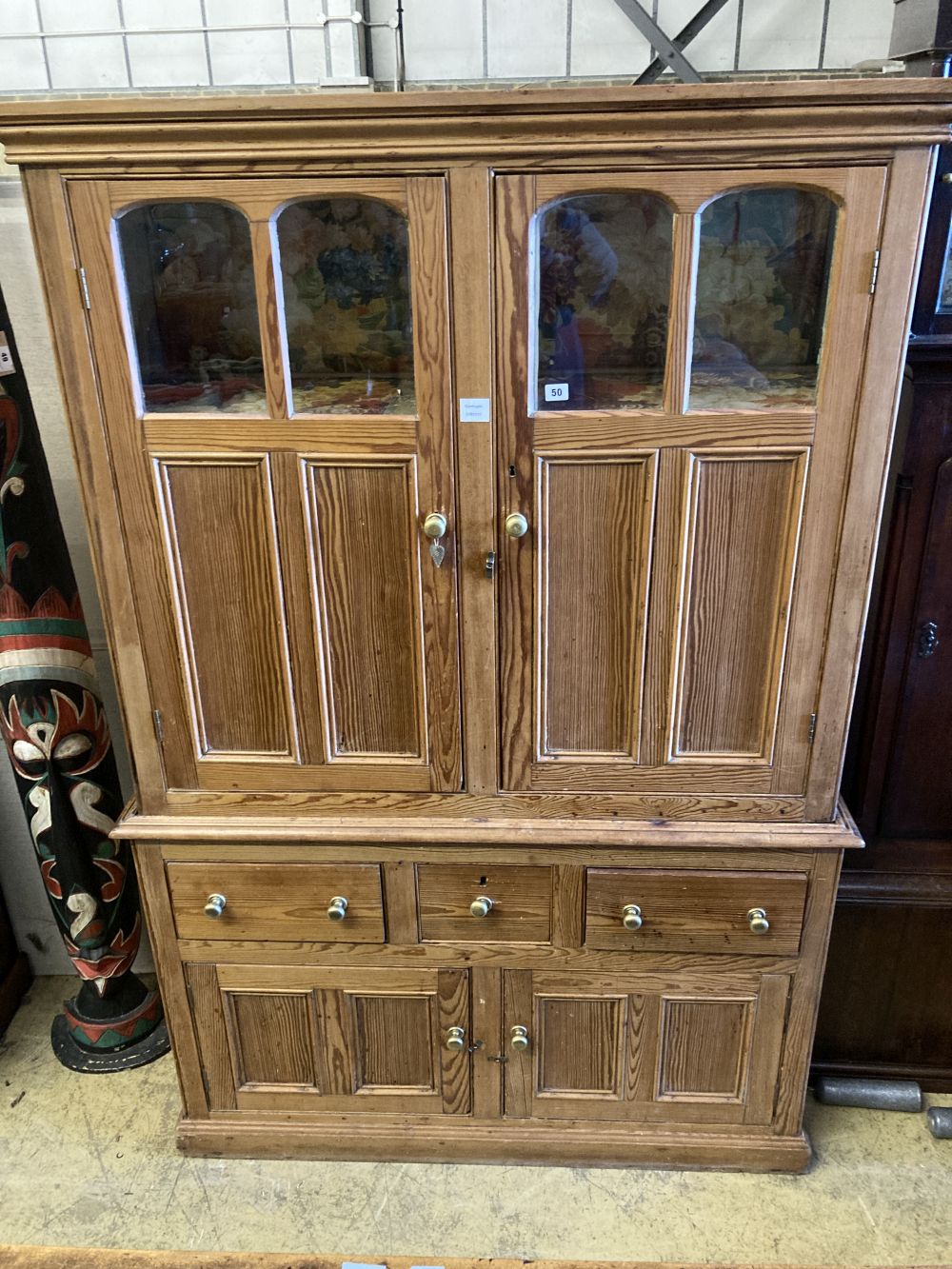 An early 19th century stripped pine cupboard, fitted with a pair of part glazed panelled doors, over three drawers and cupboards, width